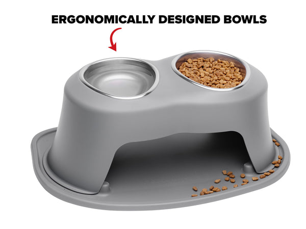 The WeatherTech Double Elevated Pet Feeding System by Weathertech features two stainless steel bowls—one with dry kibble, the other empty. A few kibbles are on the base. Text above states: ERGONOMICALLY DESIGNED BOWLS.