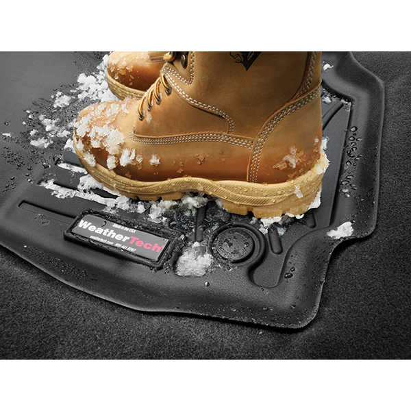 A pair of tan winter boots covered in snow rest on a WeatherTech FloorLiner for BMW 1 Series Hatch (F20/F21, 2012-2019, 1st Row), offering advanced floor protection with its textured surface amidst scattered snow and ice.