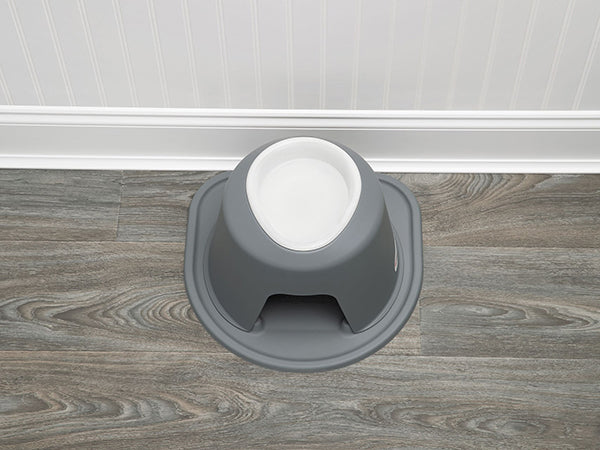 The WeatherTech Single Elevated Pet Feeding System by WeatherTech, in gray and white, sits spill-proof with a wide base on a wood-look floor against a white wainscoted wall.