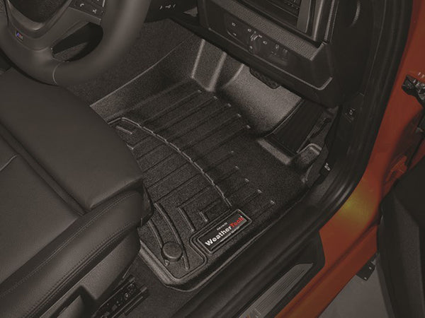 Close-up of the driver’s side floor with a black WeatherTech Floorliner for BMW 1 Series Hatch (F20/F21, 2012-2019, 1st Row), black leather seat, part of the dashboard, and an orange door frame—all protecting your interior carpet.