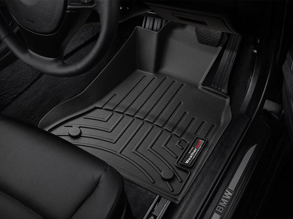 Close-up of a WeatherTech FloorLiner for BMW 5 Series Sedan/Wagon (2014-2017, F10/F11), installed on the drivers side. Ridged grooves and precise fit protect under the pedals and door sill labeled BMW.