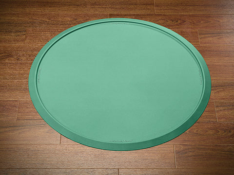 The Weathertech Christmas Tree Mat - Coloured Box is a round green silicone mat with a raised edge and smooth surface, featuring subtle rim text for reliable floor protection during the holidays. It sits neatly on wooden floors.
