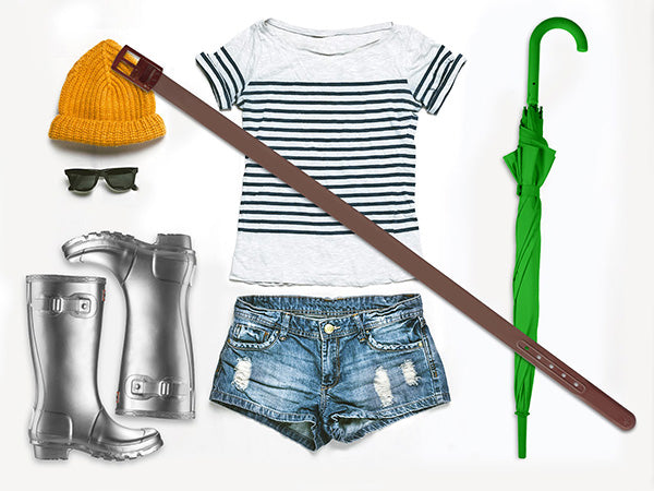 A striped t-shirt, denim shorts, gray rain boots, yellow knit hat, sunglasses, green umbrella, and a Weathertech WeatherTech Star Belt are laid out flat on a white background.