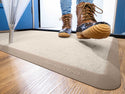 A person in brown winter boots steps onto a WeatherTech Carpet Mat by Weathertech near a blue door, placing a wet umbrella on the mat to keep the floor clean and dry from dirt and moisture.
