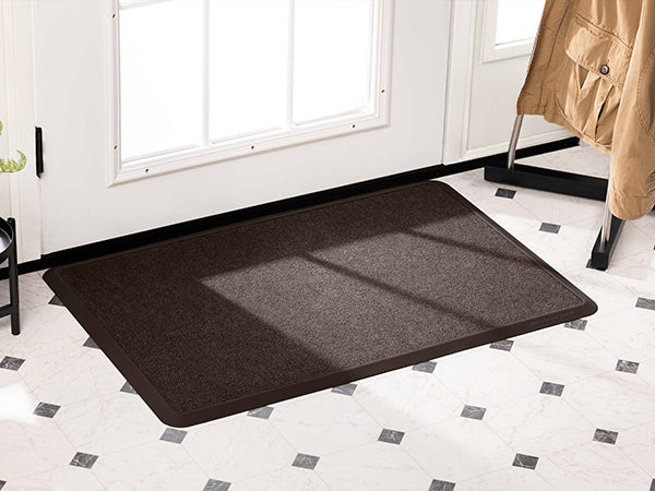 A WeatherTech Carpet Mat from Weathertech sits on white tile flooring with black diamond patterns in front of a white door with glass panels, while a beige coat hangs on a rack nearby.