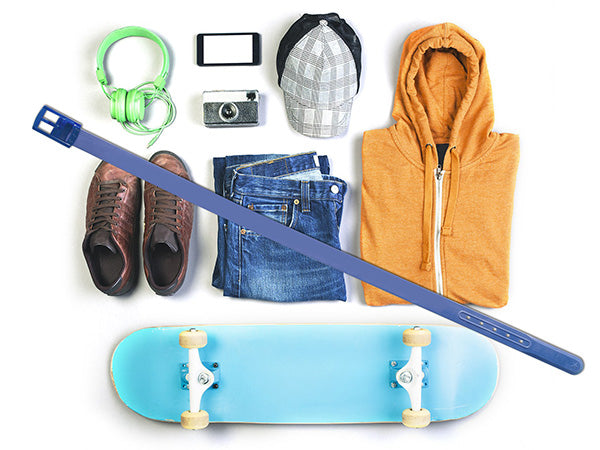 Flat lay of casual items: green headphones, smartphone, cap, orange hoodie, brown shoes, vintage camera, blue jeans, blue skateboard, and the WeatherTech Star Belt by Weathertech placed diagonally across the image.