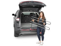 A woman stands behind an SUV with the trunk open, smiling at the camera while holding a folded Weathertech Pet Barrier. The cargo area of the vehicle is visible.