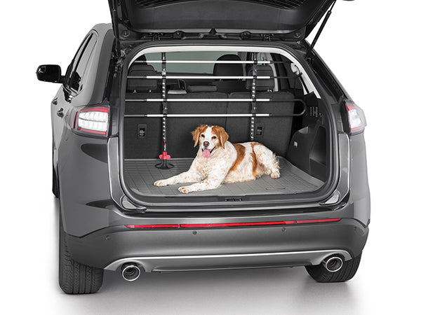 A brown and white dog lies in the cargo area of an SUV with its rear hatch open. The trunk features a protective mat and a WeatherTech Pet Barrier installed behind the back seats for added safety.