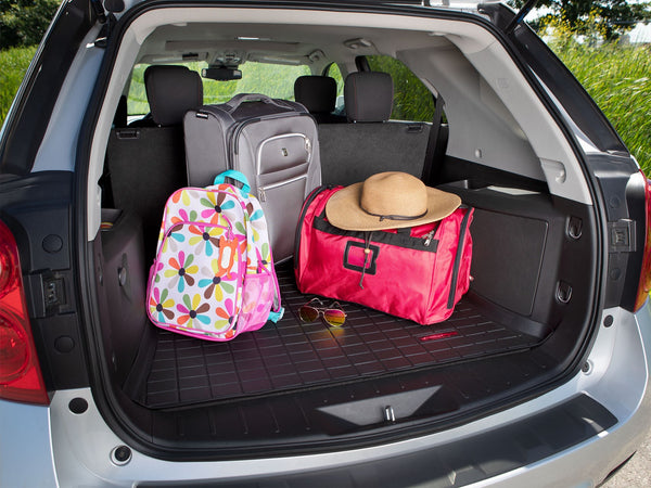 Open the trunk of a MINI Countryman (U25) lined with the Weathertech CargoLiner in black, packed with a gray suitcase, colorful floral backpack, red duffel bag, straw hat, and sunglasses—ready for your next adventure.