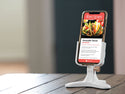 A Weathertech DeskFone White holds a smartphone on a wooden table indoors, displaying an avocado taco recipe with photos and ingredients—making for a convenient desktop phone holder setup.
